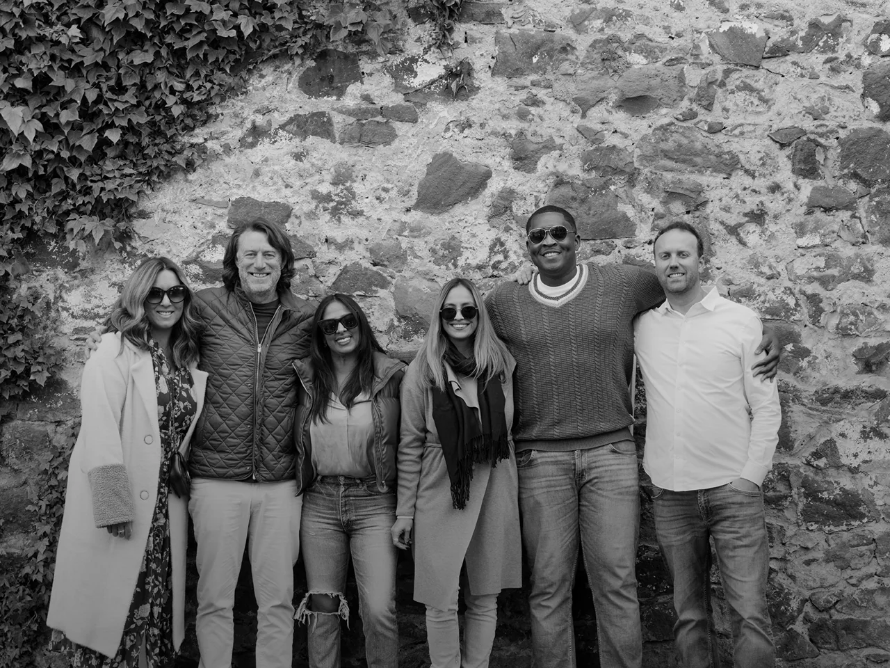 A group gathered beside an ivy-covered stone wall.