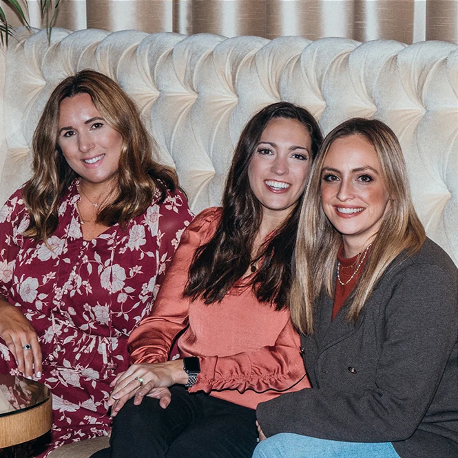 Three team members smiling together on a sofa.