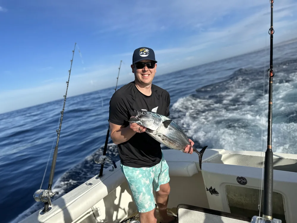 Holding a fish on deck with the ocean behind.