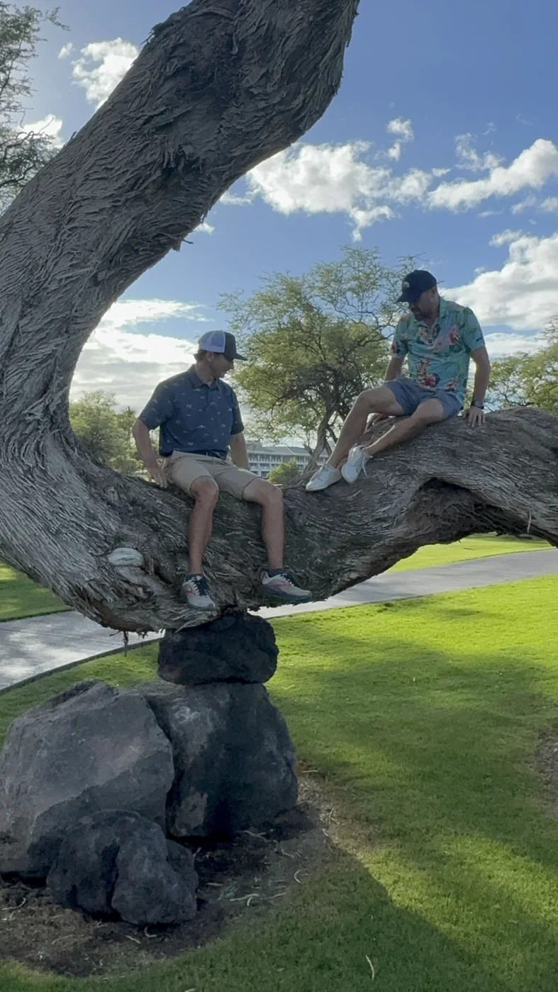 Two people sitting on a broad tree branch.